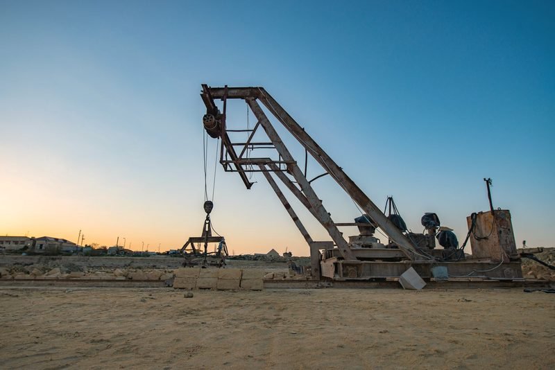 A rusted lifting boom in a dirt yard at sundown