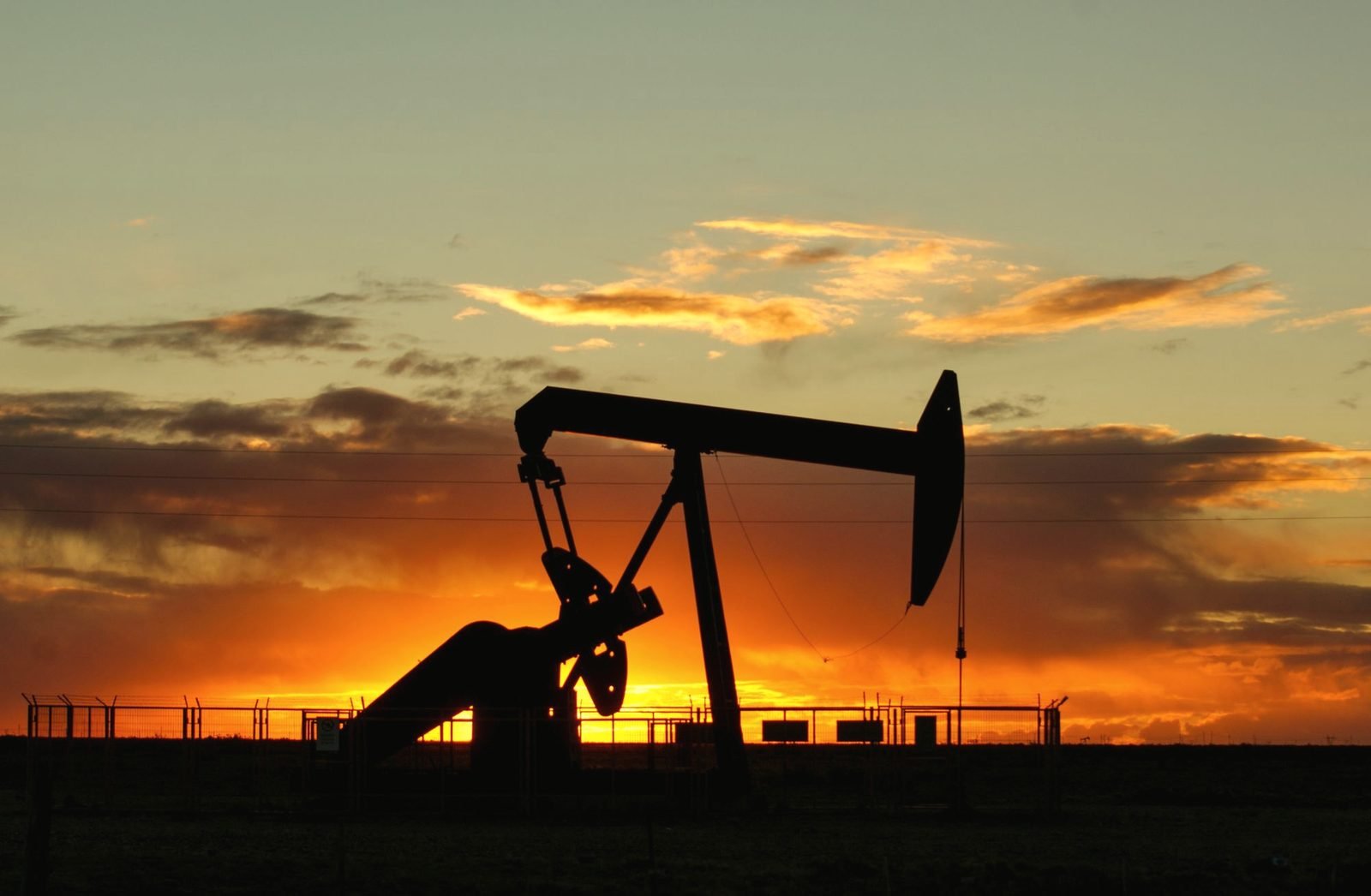 A pumpjack in silhouette against an orange sunset over flat ground