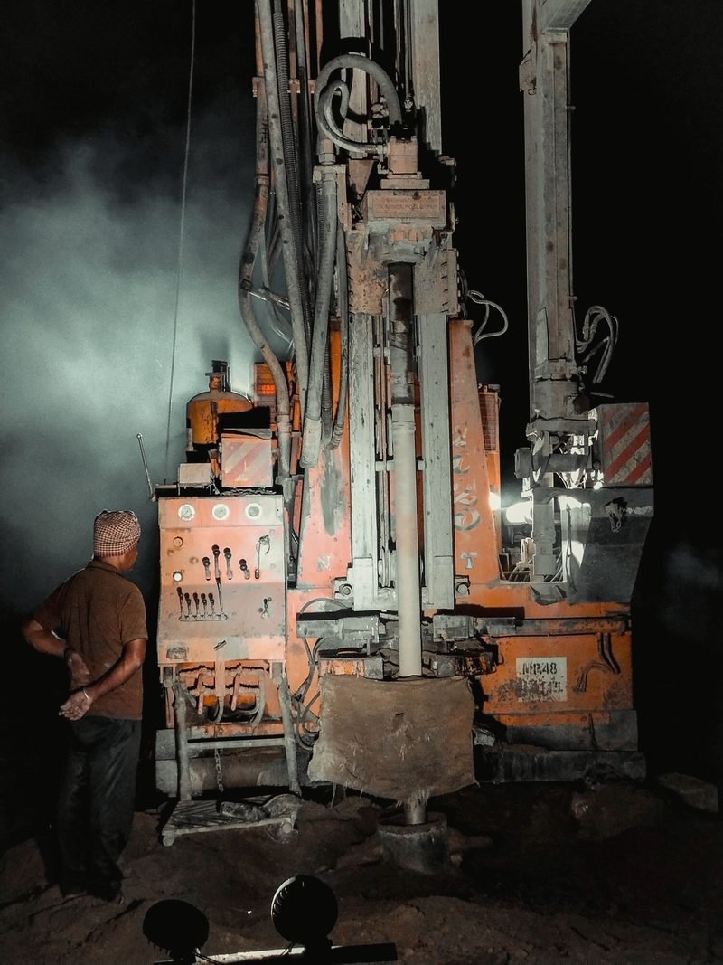 A rig working at night under floodlights, a hand standing at the controls seen from behind